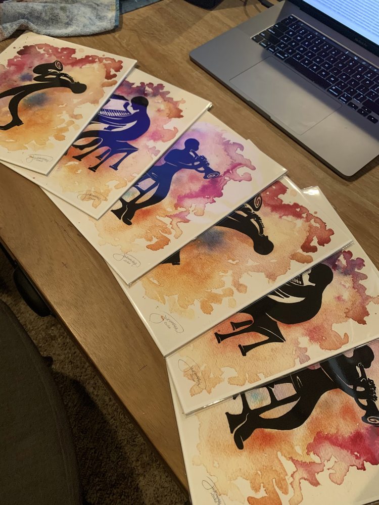 A fanned-out row of signed prints of jazz musicians in black silhouette over warm watercolor splashes